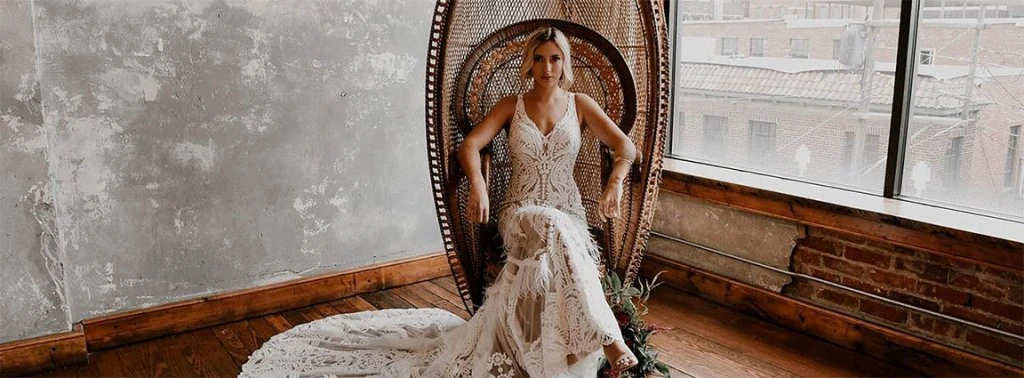 Boho Bride wearing her Reece wedding dress from designer All Who Wander, sitting in a peacock rattan chair