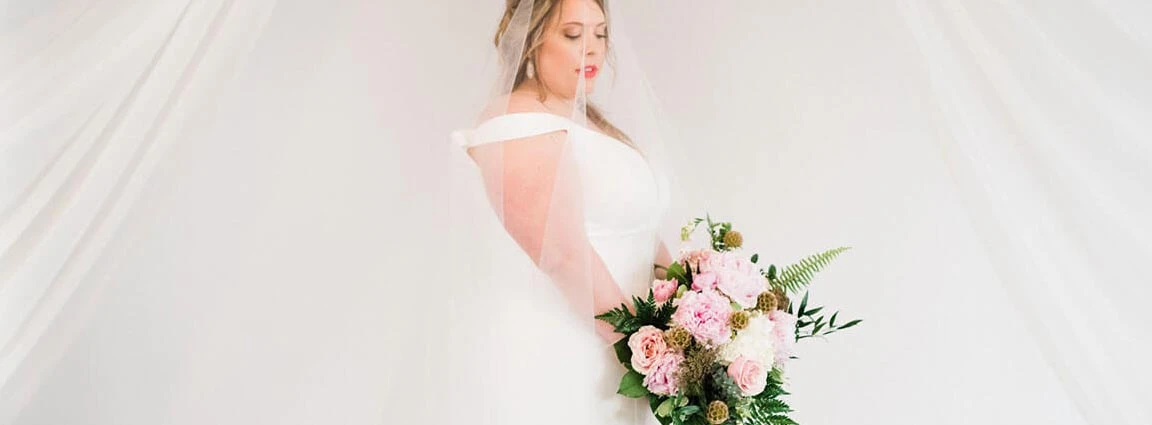 Plus size bride wearing a simple, off the shoulder wedding gown from her local True Society bridal shop.