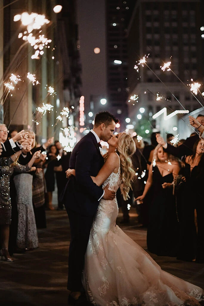True Bride Brittany kissing her husband outside under sparklers. She is wearing a wedding dress by designer Martina Liana, style 906.