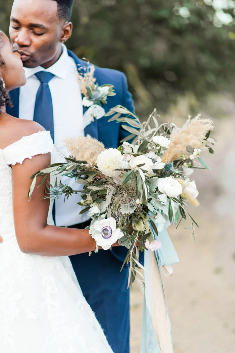 Trendy bride styled photo featuring groom and bride kissing and holding bouquet