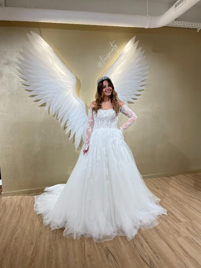 bride wearing a lace ballgown standing in front of angel wings, essense of australia d3183