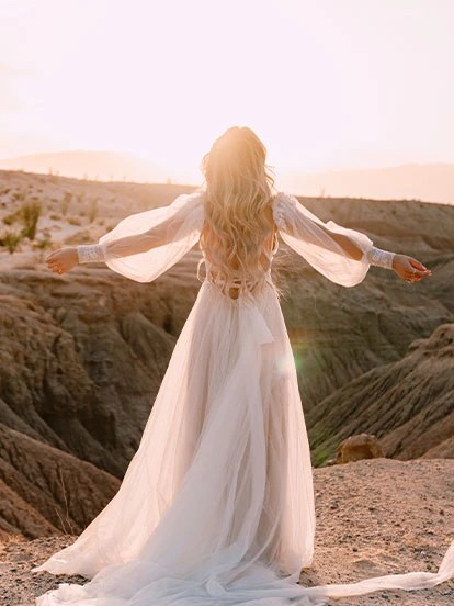 Bride faces a sunset wearing a long sleeve chiffon A-line wedding dress.