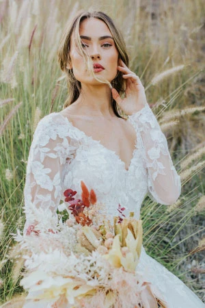 Woman with light-brown hair wearing a long-sleeve wedding dress with lace and a v-neckline.