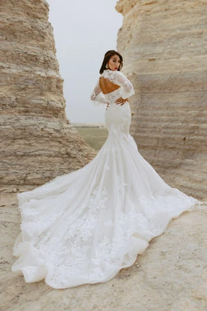 Woman with long brown hair wearing a mermaid silhouette wedding dress with an open back, lace, and long sleeves.