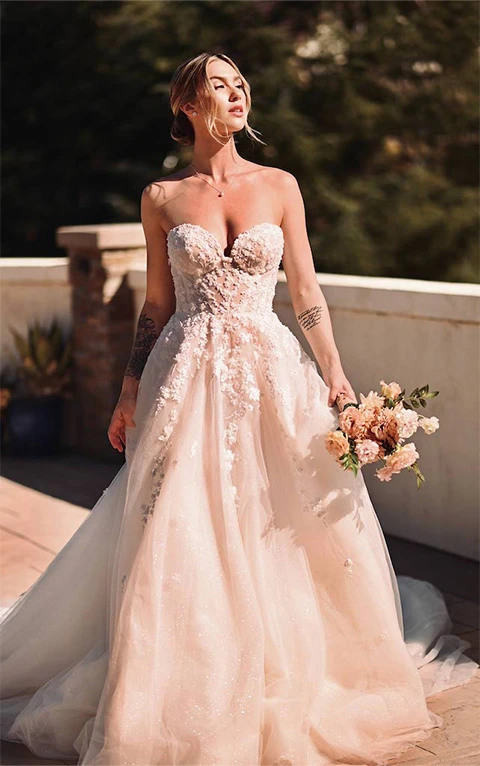 Bride wearing strapless floral princess wedding dress with sweetheart neckline stands on balcony.