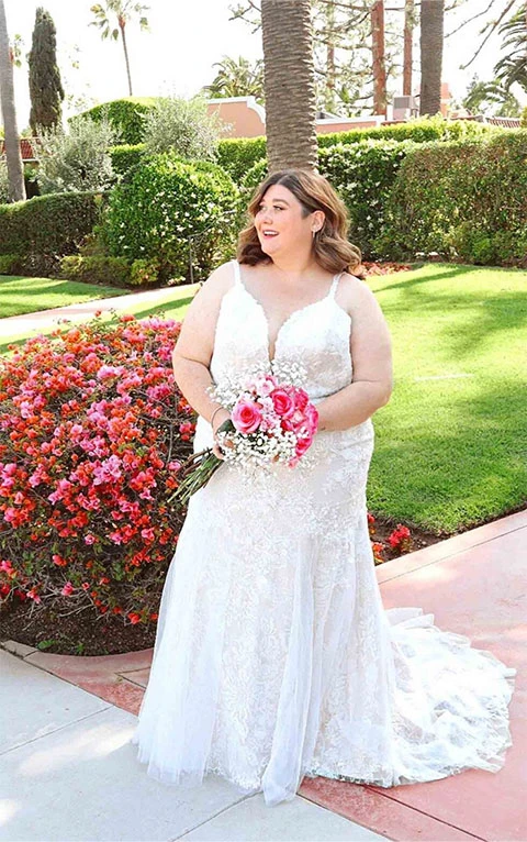 Plus sized bride wearing lace mermaid wedding dress while holding flowers