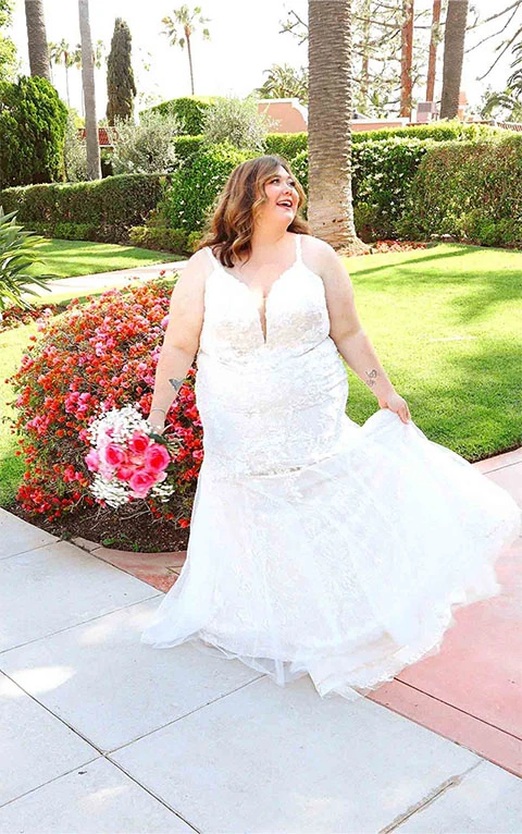 Plus sized bride wearing lace mermaid wedding dress while holding flowers