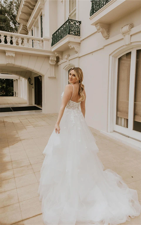 Bride looks back wearing floral lace princess wedding dress with layered tulle skirt.