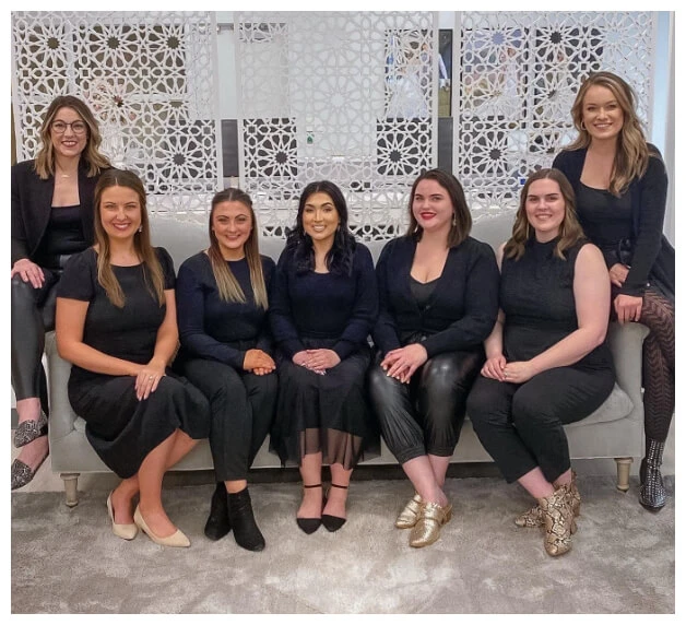 7 True Crew stylists sit on a couch at True Society Bridal Shop in Lenexa, KS.