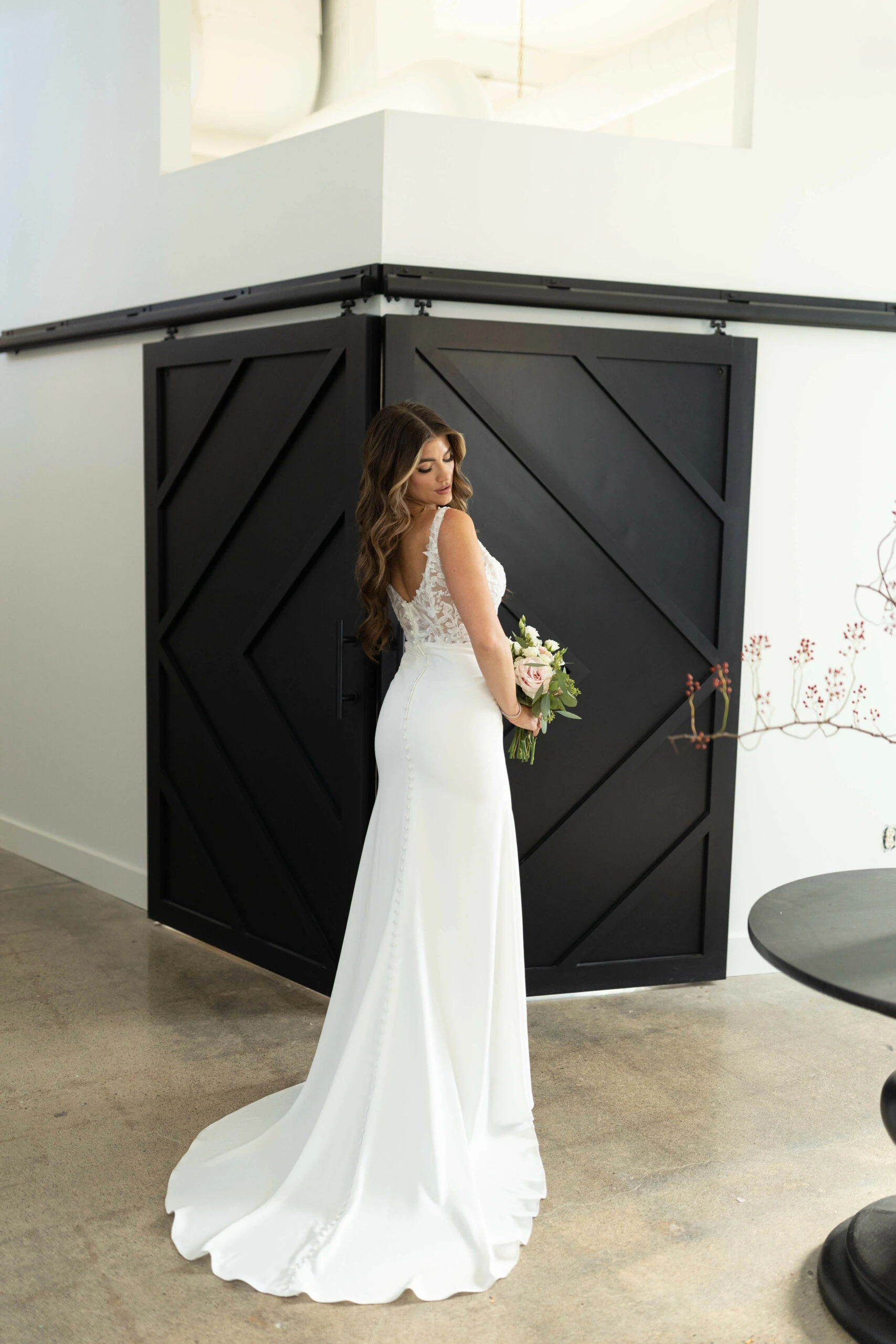 Bride in Stella York Style 7701, a lace and crepe column wedding dress with a button-back train.