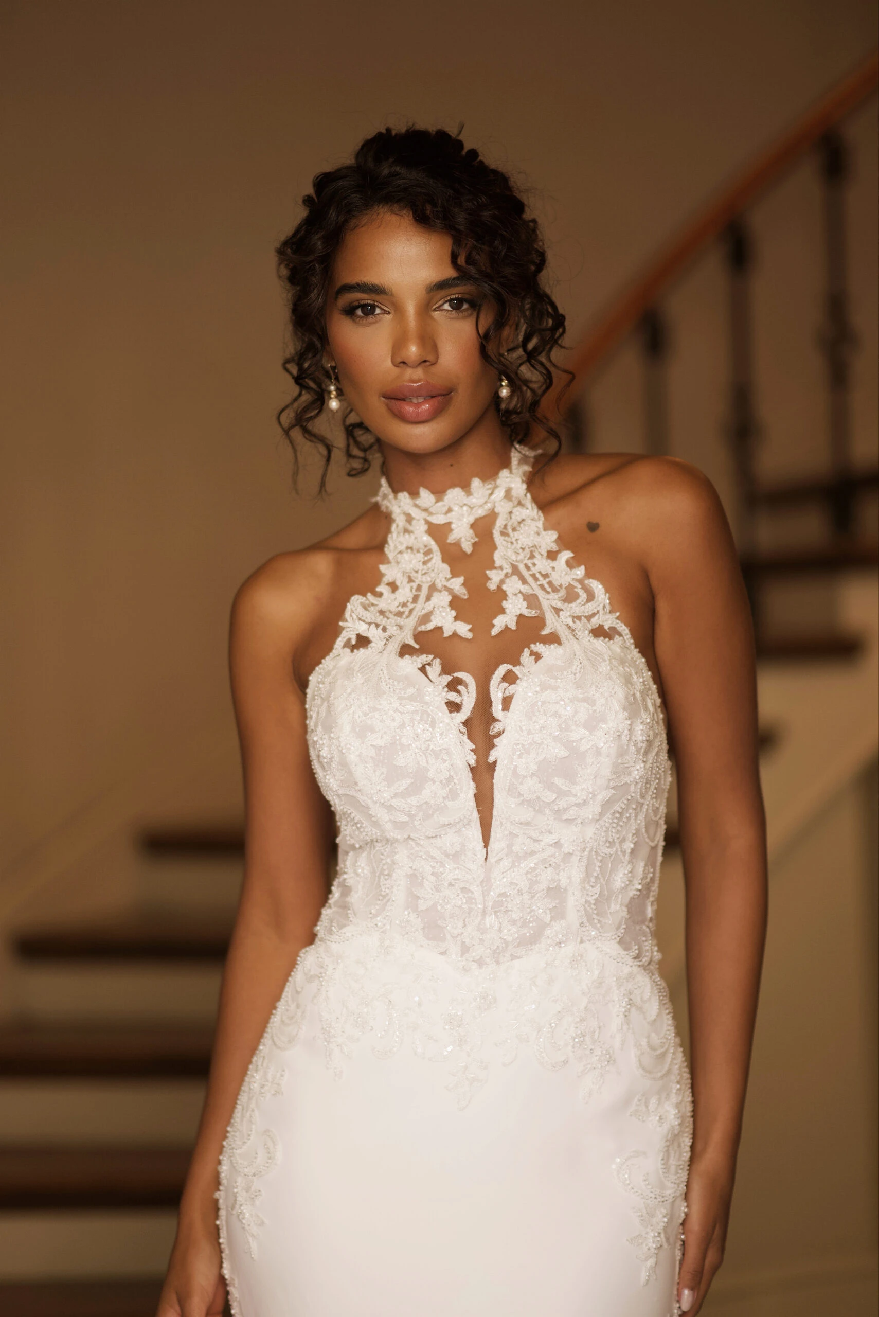 bride is standing in a doorway walking towards the camera. She is wearing Martina Liana Style 1787, which features a high lace neckline and an illusion plunging neckline.