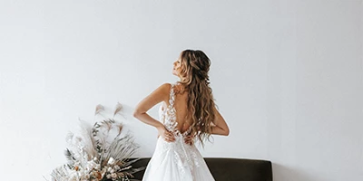 Bride wearing an open back lace wedding dress facing a wall.
