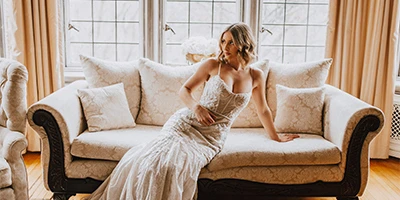 Bride wearing a lace fit-and-flare wedding dress sitting on a couch.