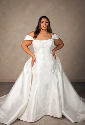 Plus size bride wearing matte lace and mikado fit-and-flare wedding dress with detachable overskirt and scoop neckline
