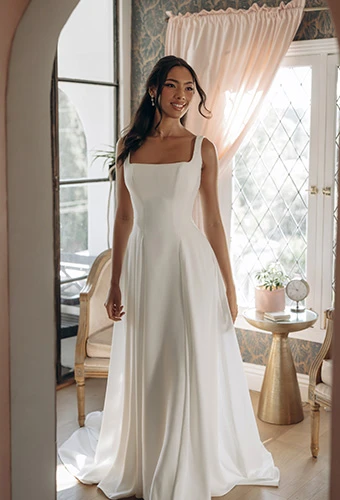 Bride wearing a modern A-line wedding dress with square neckline, low square back, crepe fabric, and button detail.