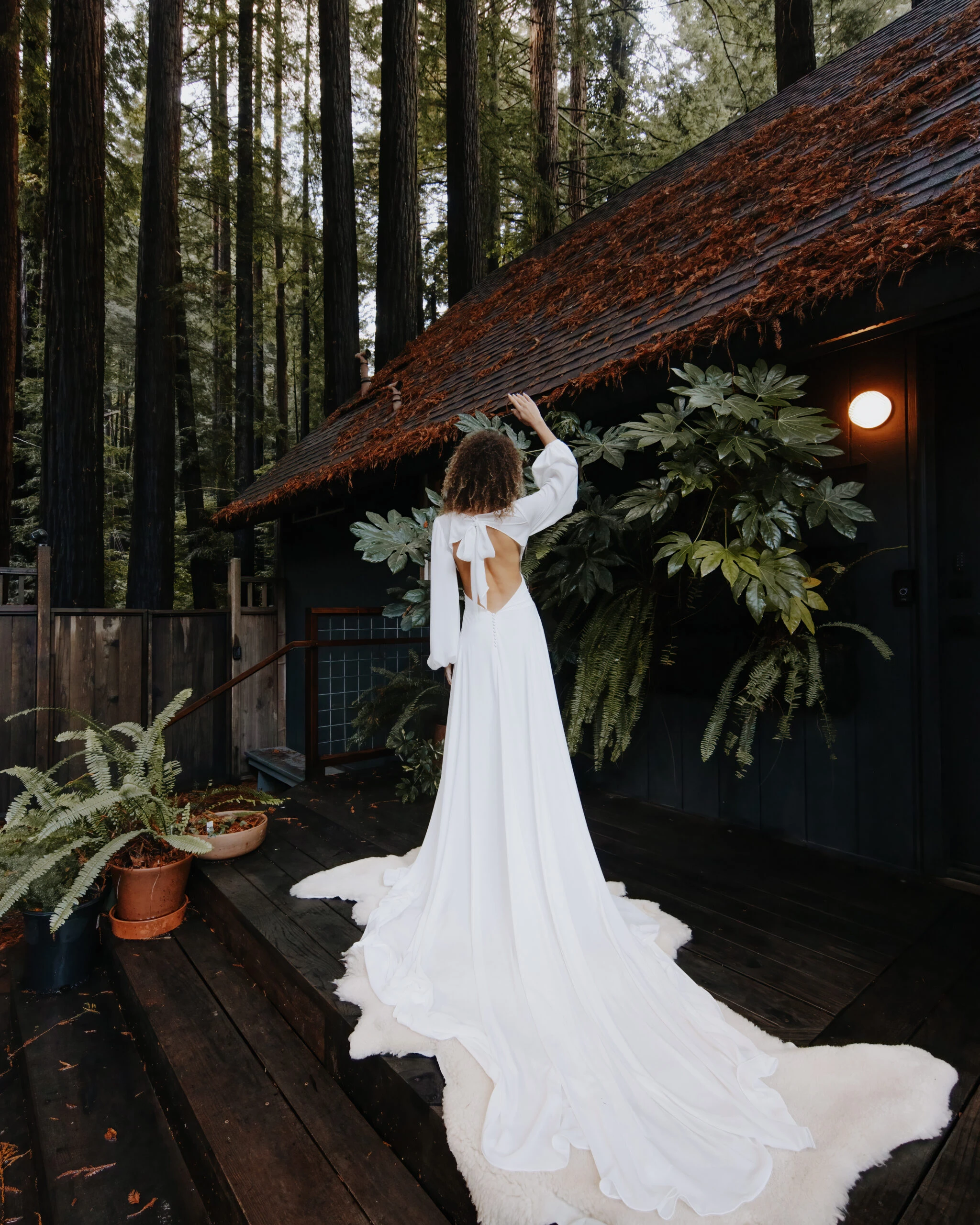 Back of bride wearing an open back long sleeve wedding dress in a forest