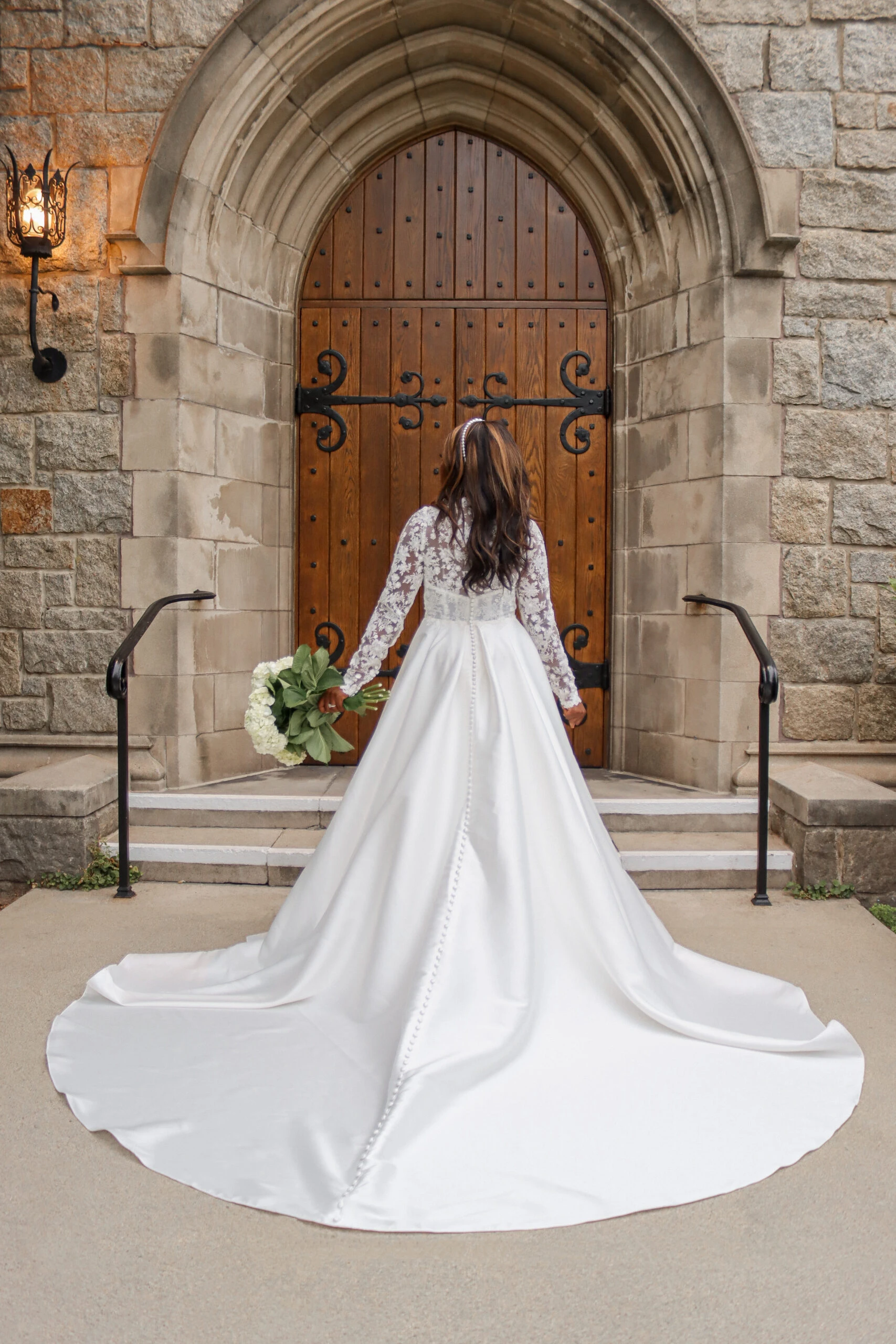 back of bride bride standing in front of a church wearing long sleeve high neck lace wedding dress