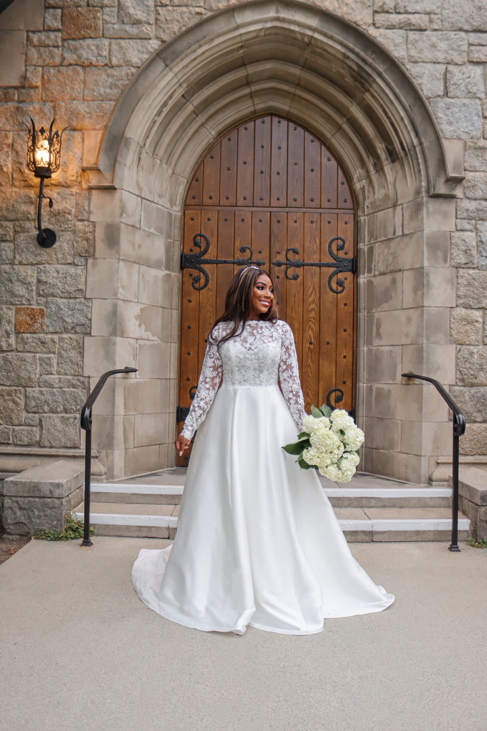 bride standing in front of a church wearing long sleeve high neck lace wedding dress
