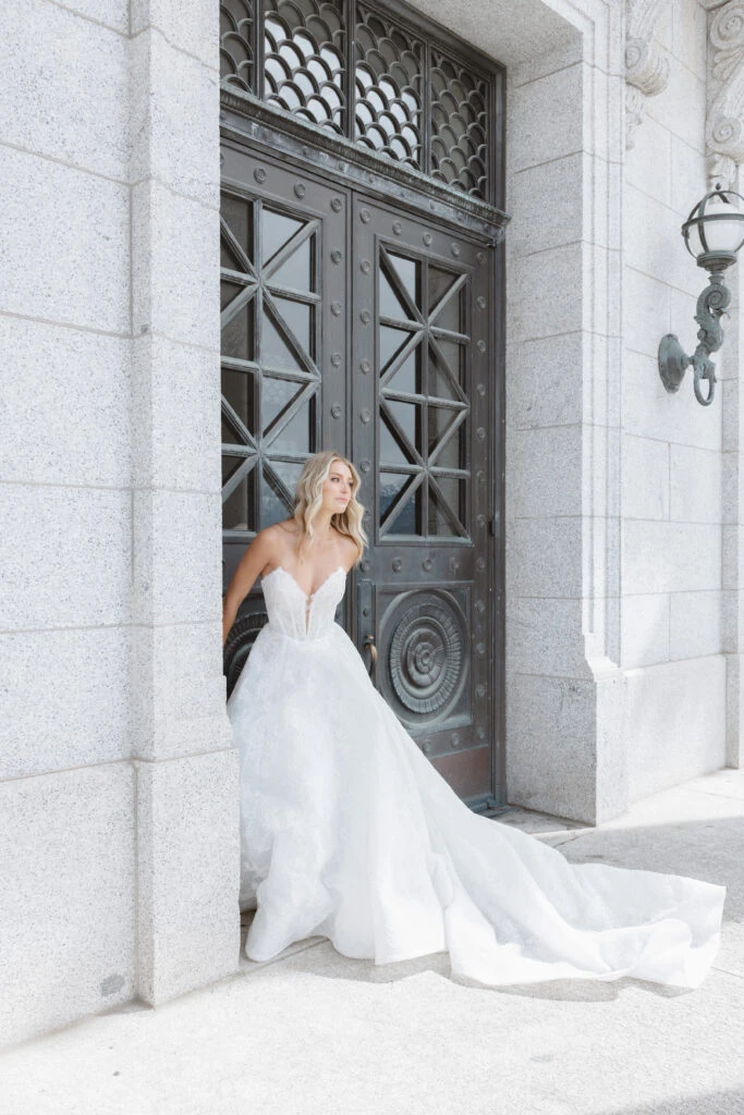 Bride leaning against door wearing a lace strapless wedding dress