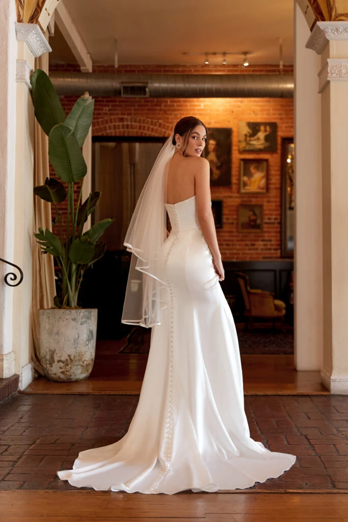 Back of bride wearing a simple strapless column wedding dress with a finger tip length veil