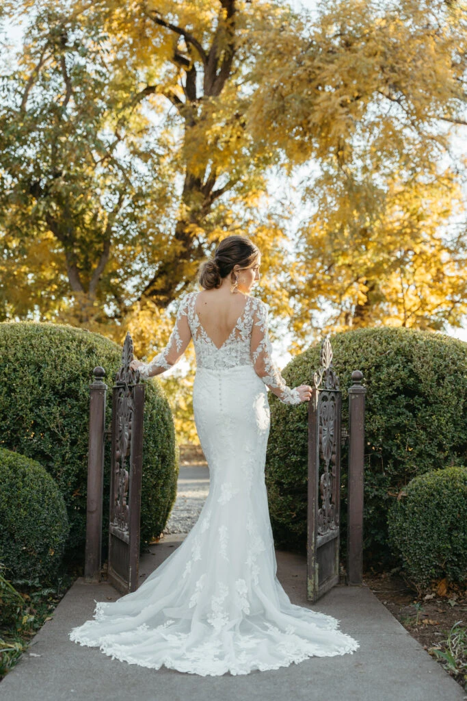 Back of Bride wearing long sleeve lace wedding dress standing between bushes