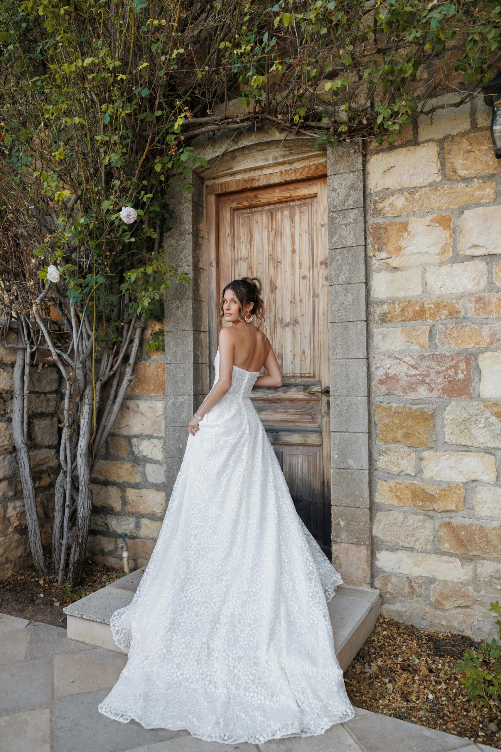 Back of bride wearing lace strapless ballgown wedding dress posing in front of a rustic wooden door.