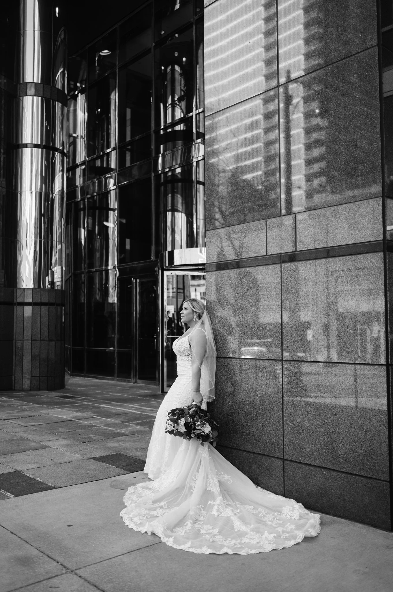 Bride holding flowers leaning against a building
