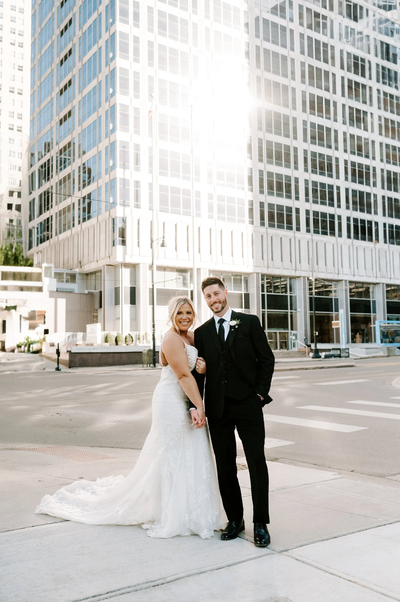 Bride and groom holding hands outside next to a skyscraper