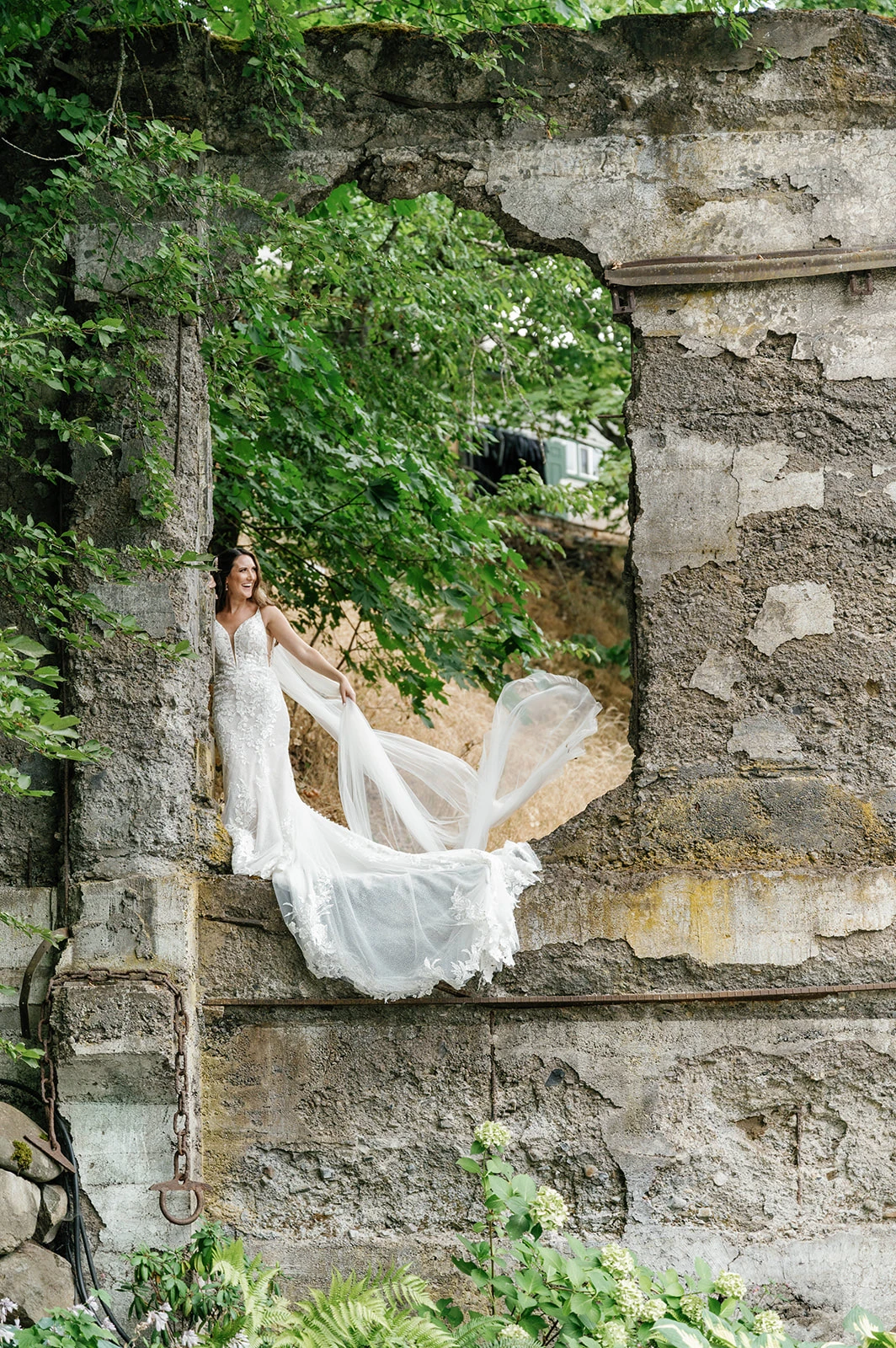 Bride posing on a rustic stone structure with the their long veil flowing down