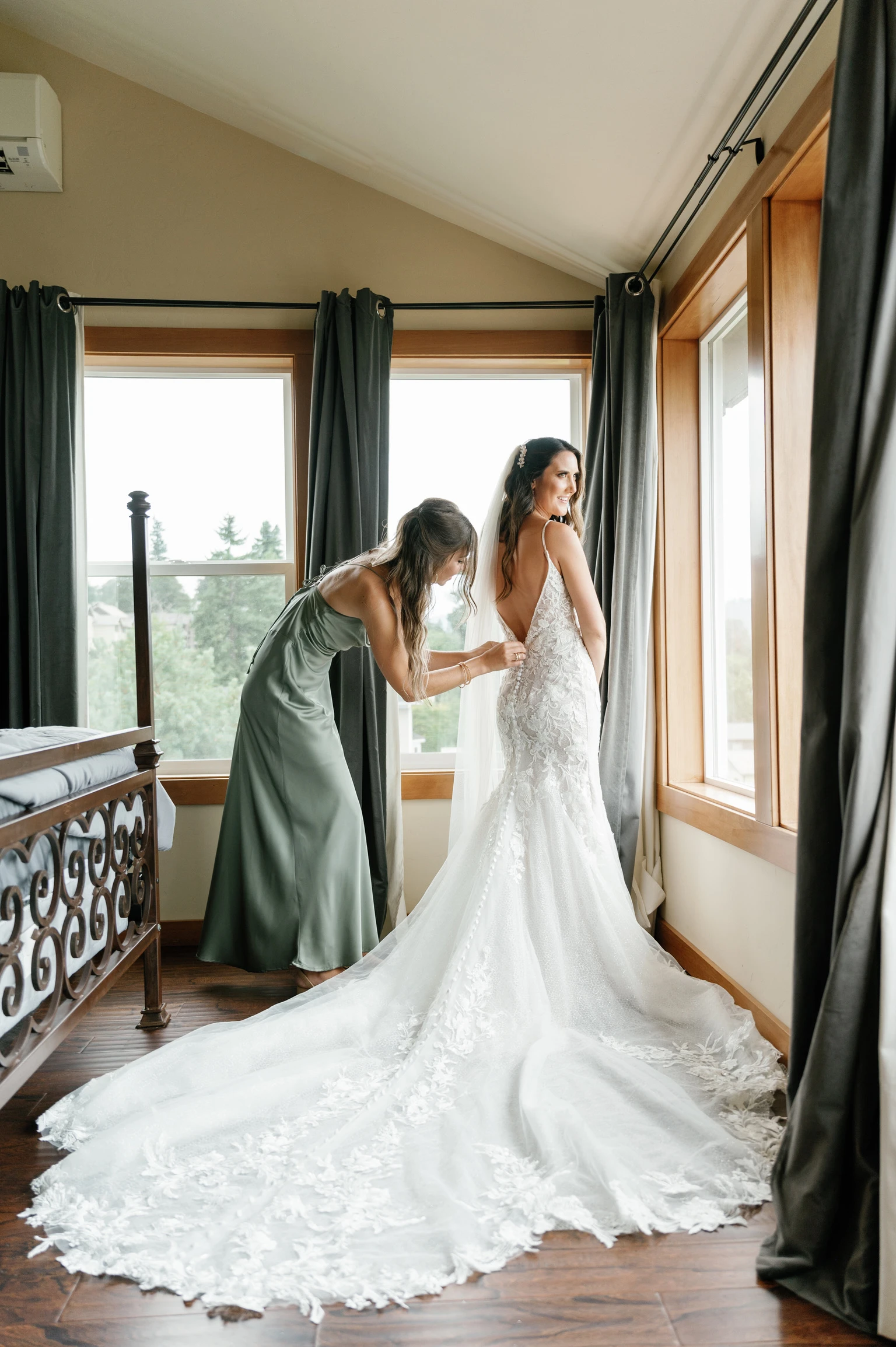 Bride getting ready with the help of a bridesmaid, showcasing a lace wedding dress with a long train