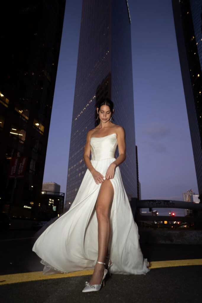 Bride wearing a off the shoulder wedding dress with a high slit in a city