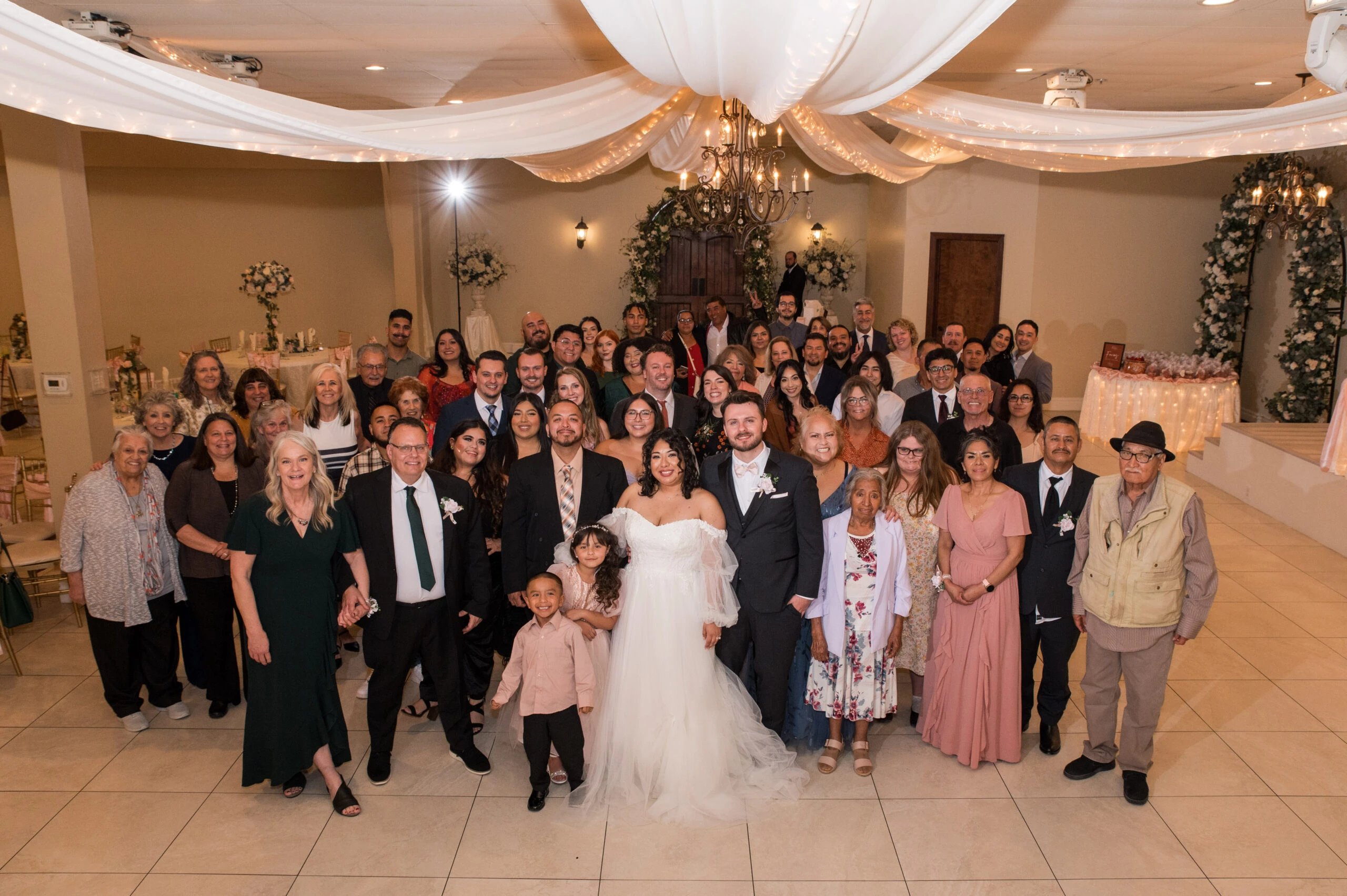 The bride and groom stand surrounded by guests at a wedding reception venue