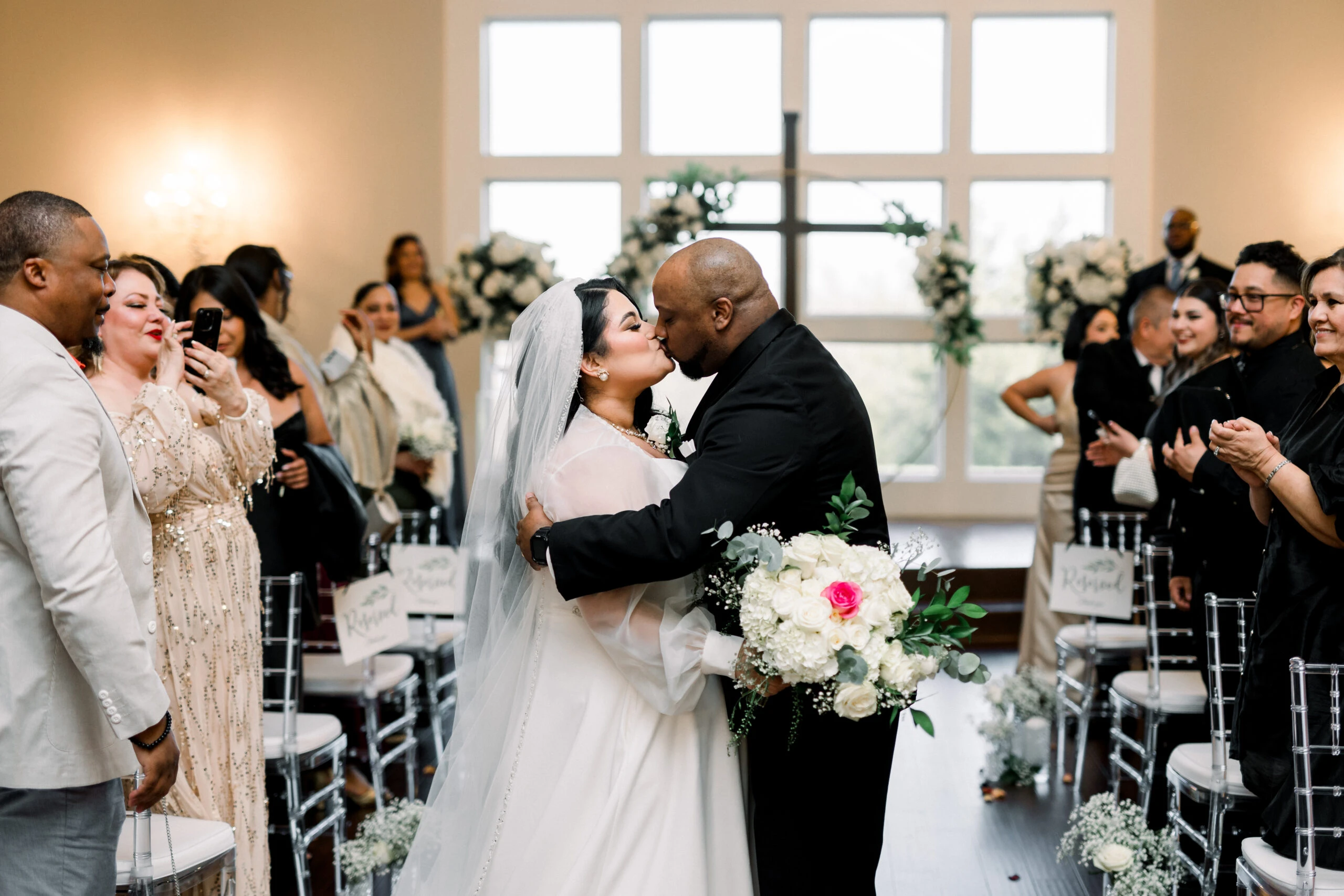 Bride and groom kissing in the aisle surrounded by wedding guests.