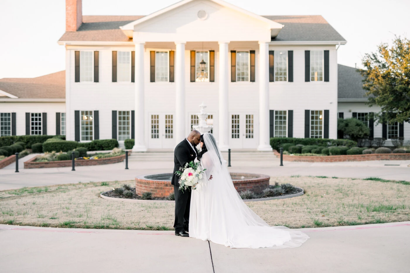 Bride and groom kissing in front of a large white house.