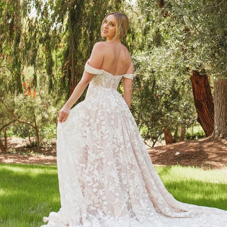 bride wearing lace a-line wedding dress holding skirt out in front of trees.