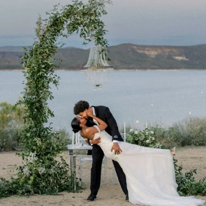 couple kissing in front of ocean under a leafy arch