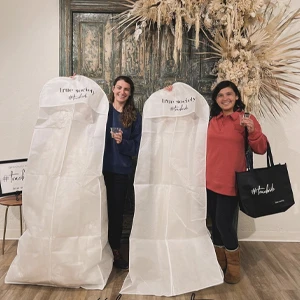 brides smiling and holding up their garment bags when picking up their wedding dresses.