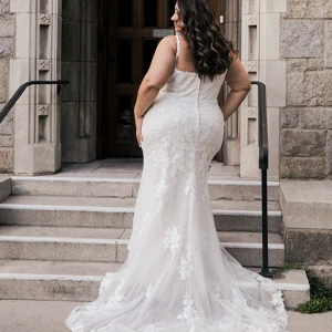 plus size bride posing on stairs in a mermaid wedding dress with a shaped train.