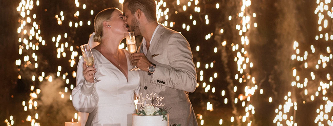 bride and groom kissing while holding champagne and surrounded by sparklers.