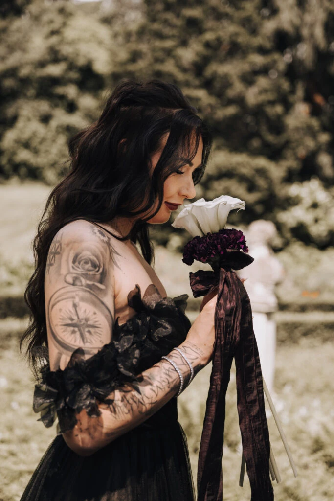 Bride wearing an off-the-shoulder black lace wedding dress smelling a bouquet flowers