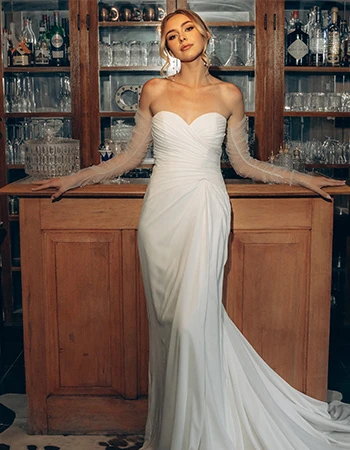 Bride wearing a strapless wedding gown and tulle gloves leaning against a bar.