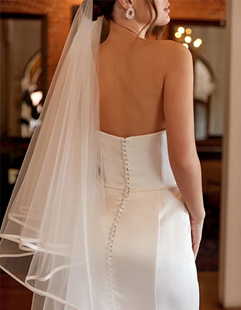 Bride wearing a strapless wedding dress and finger tip length veil with with a silk trim