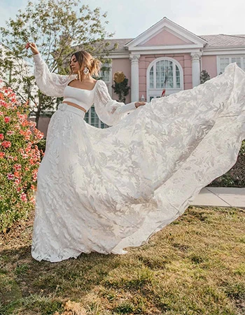 Bride wearing a two piece wedding dress with a belt and bell sleeves while throwing up the train in the air