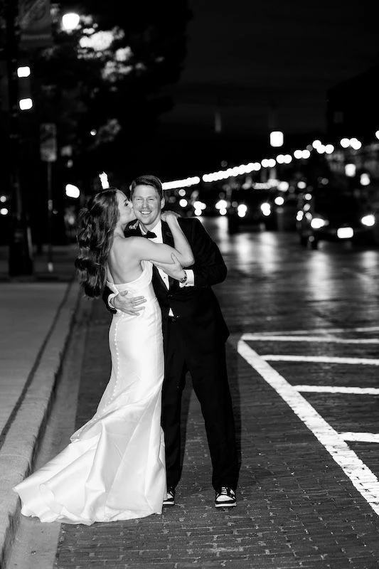 Bride and groom embracing on the side of the street.