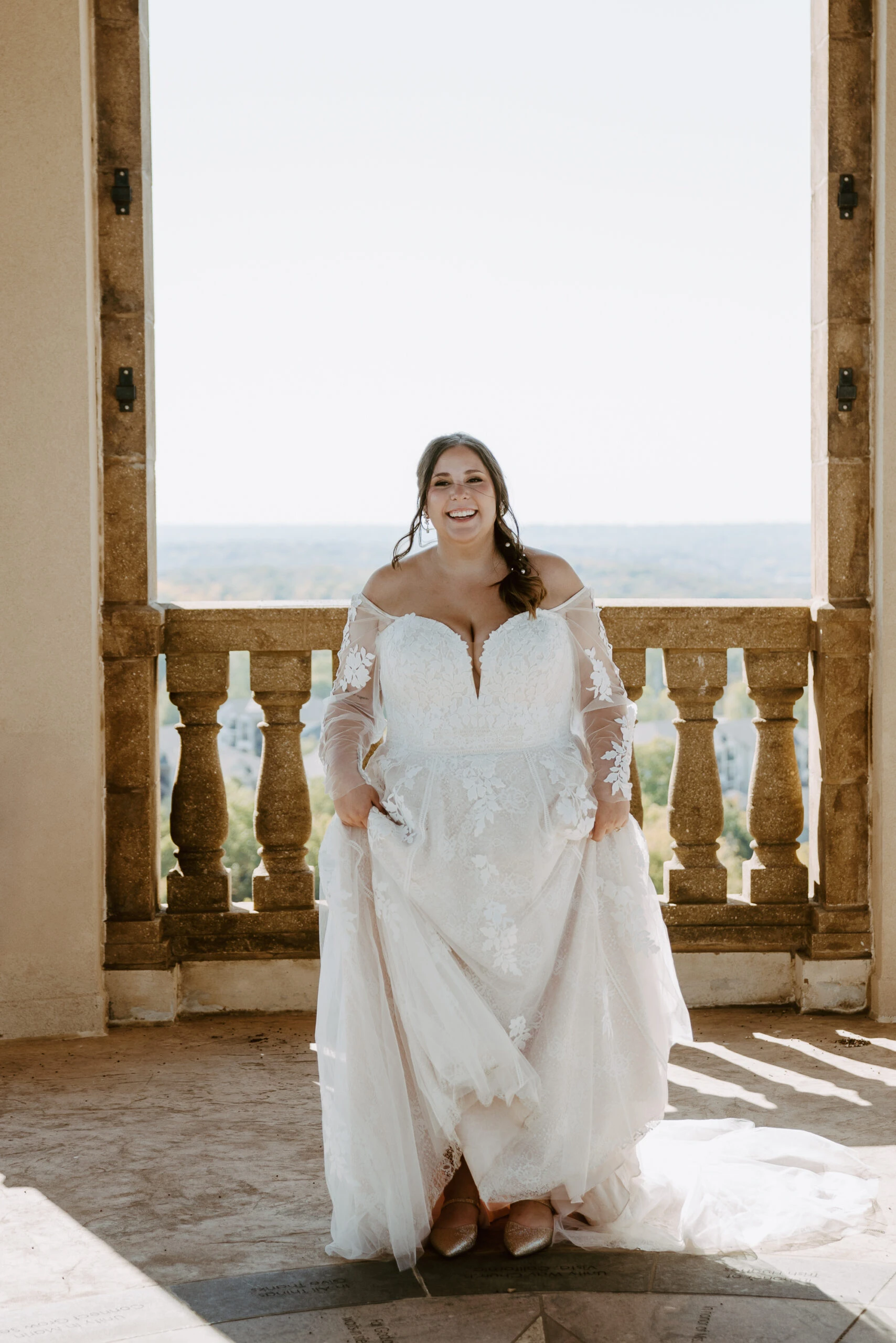 true bride Rachel holding her wedding dress skirt and smiling in front of pillars