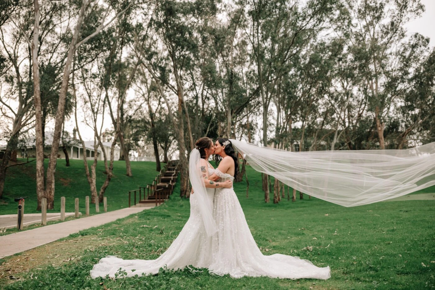 Brides kissing wearing lace wedding dresses standing in a garden