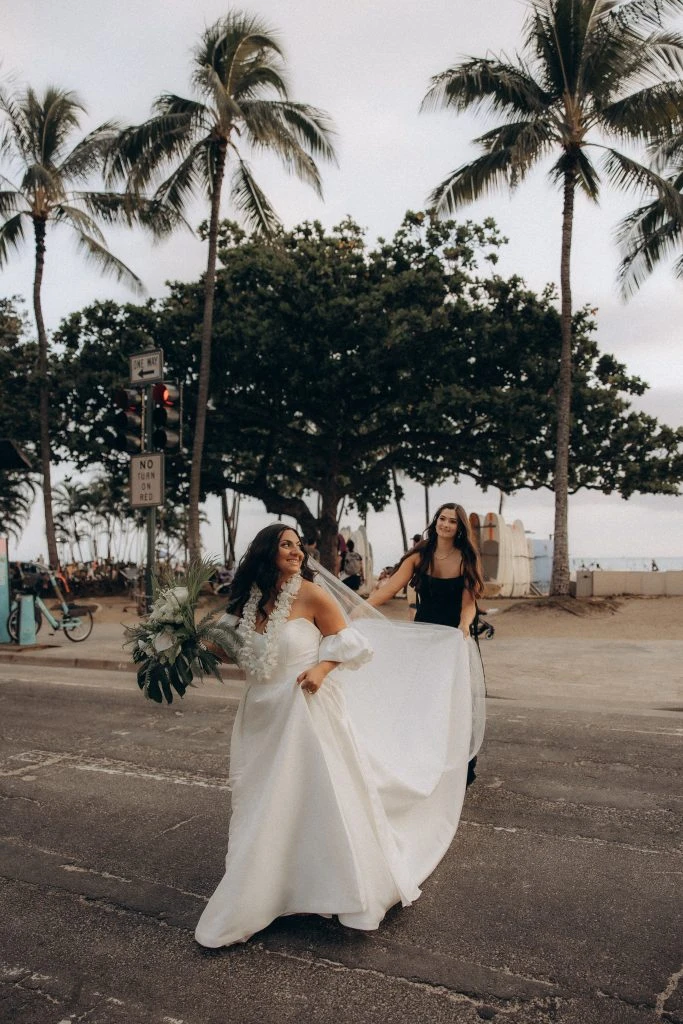 true bride hana walking across street while bridesmaid holder her train and veil - 7601 by Stella York