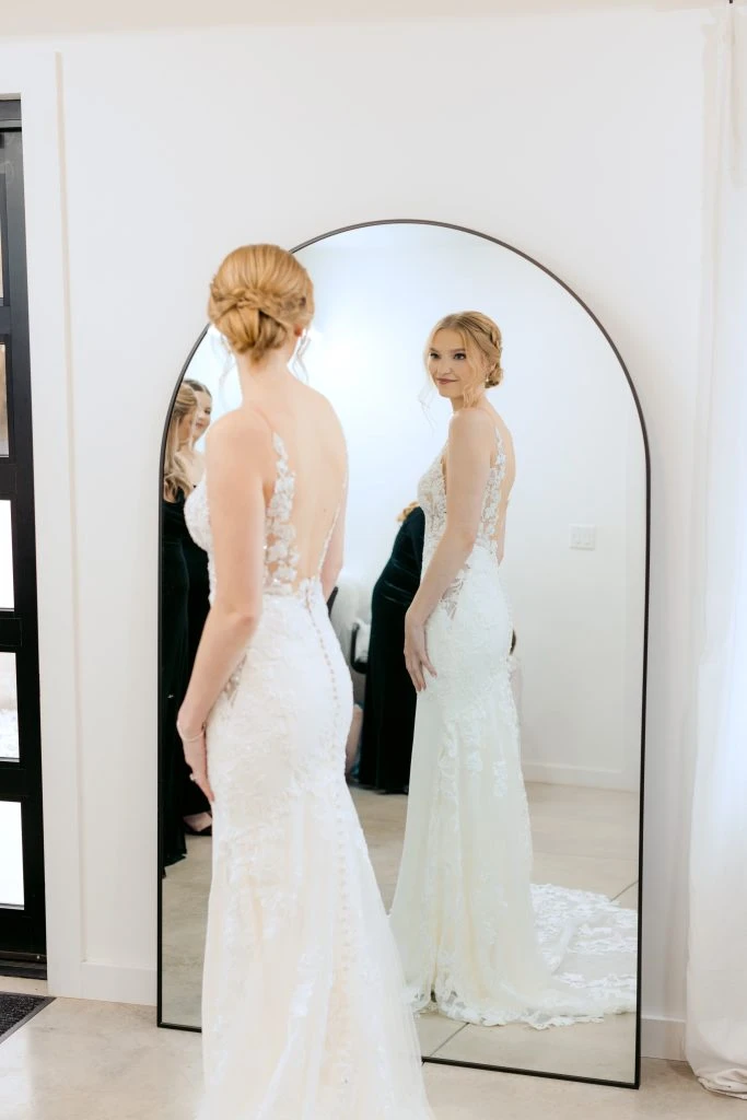 Bride with lace wedding dress on standing in front of mirror