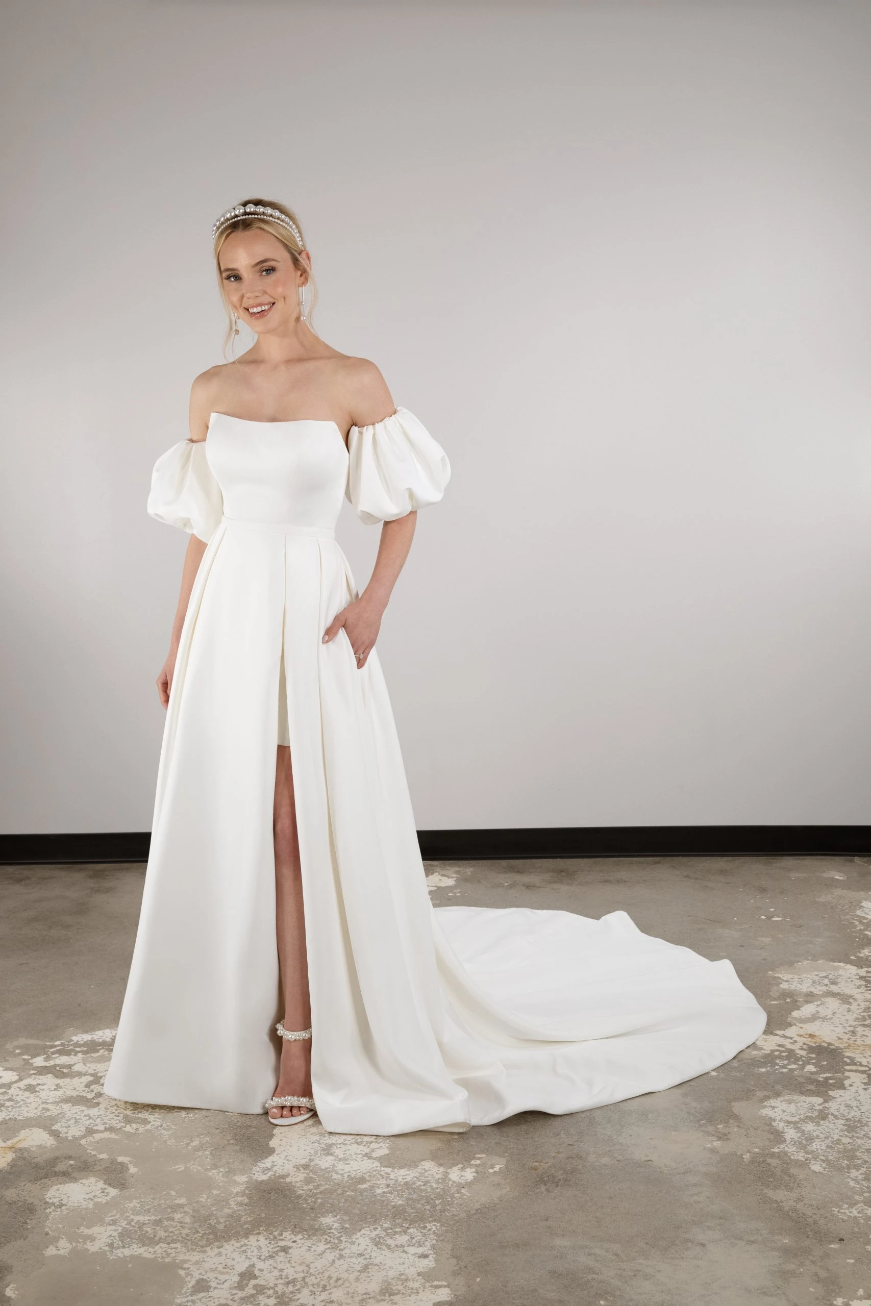 model posting in front of blank wall in a simple wedding dress with puff sleeves and pockets - D3957 by Essense of Australia