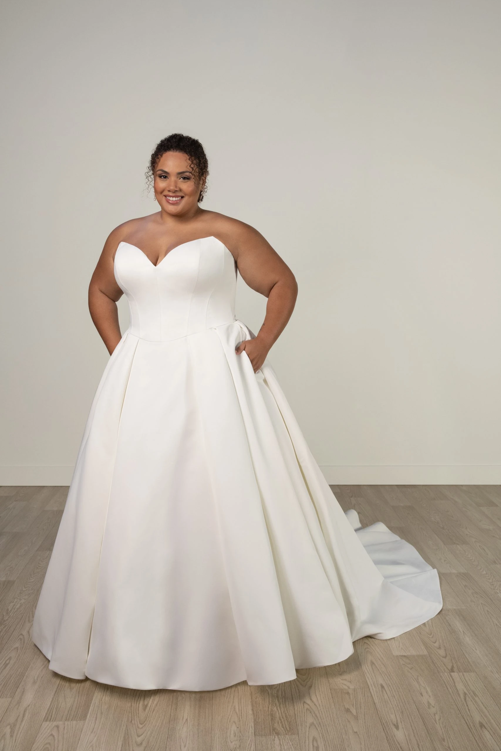 plus size model posing in front of plain wall in simple ballgown wedding dress with pockets - 8033+ by Stella York